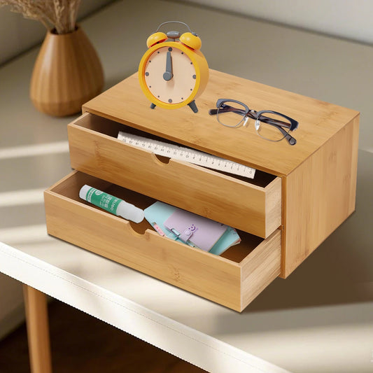 Bambus-Organizer mit zwei geöffneten Schubladen auf einem Tisch mit Wecker und Brille